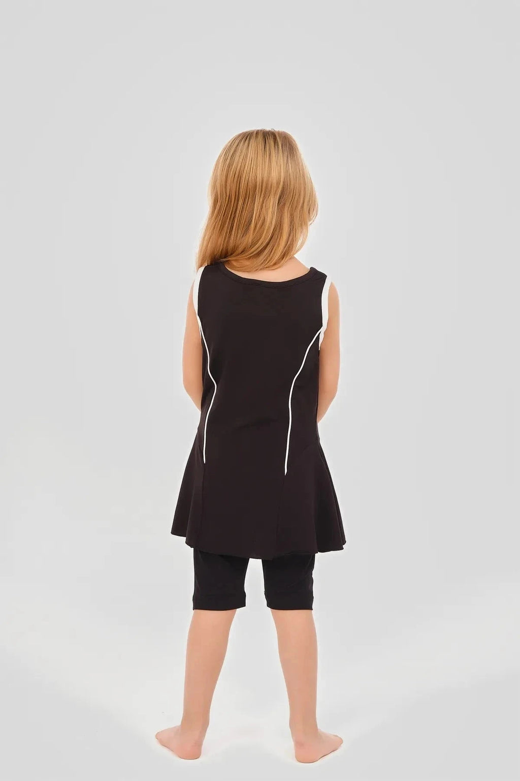 Back view of a young girl in a black modest swim dress with white piping.