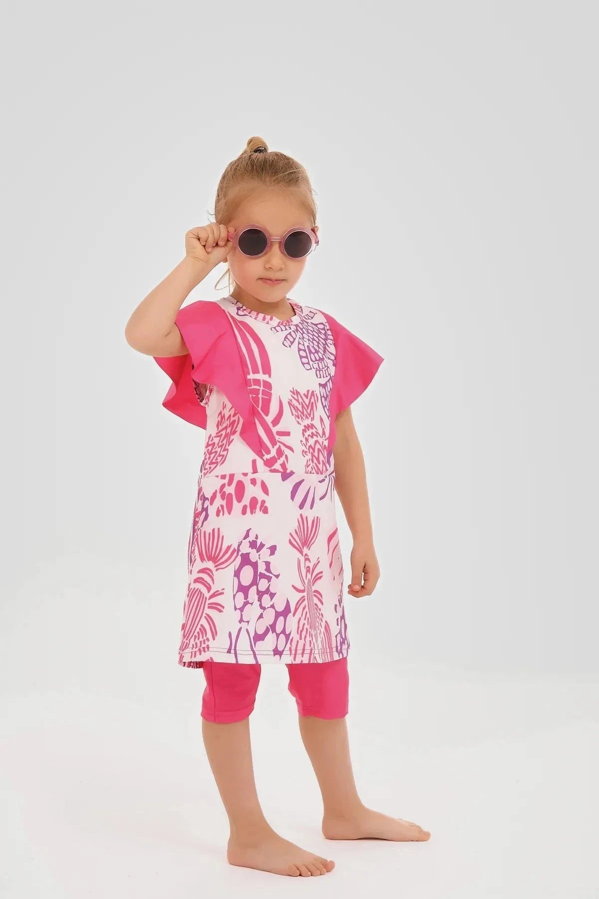Young girl in pink floral print burkini dress adjusting sunglasses