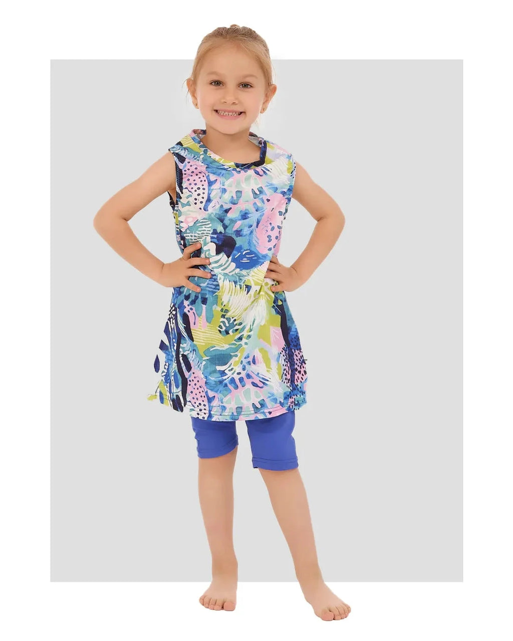 Young girl in a floral print burkini dress and blue leggings, front view.