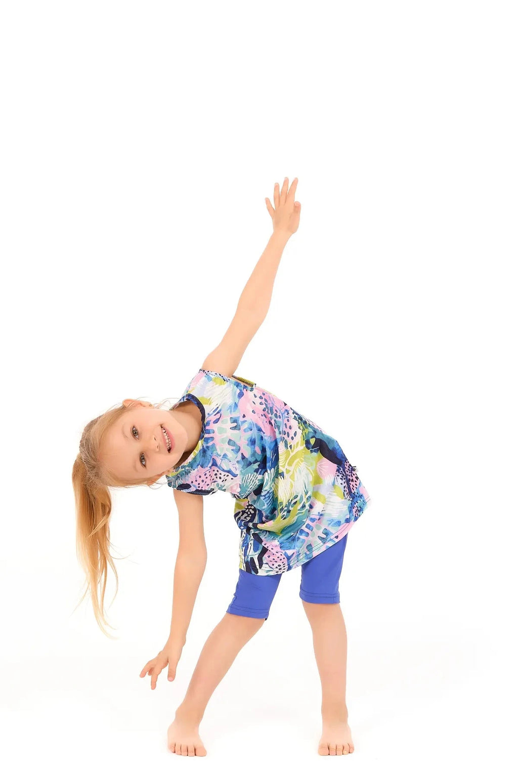 Young girl in a floral print burkini dress and blue leggings, in a playful pose.