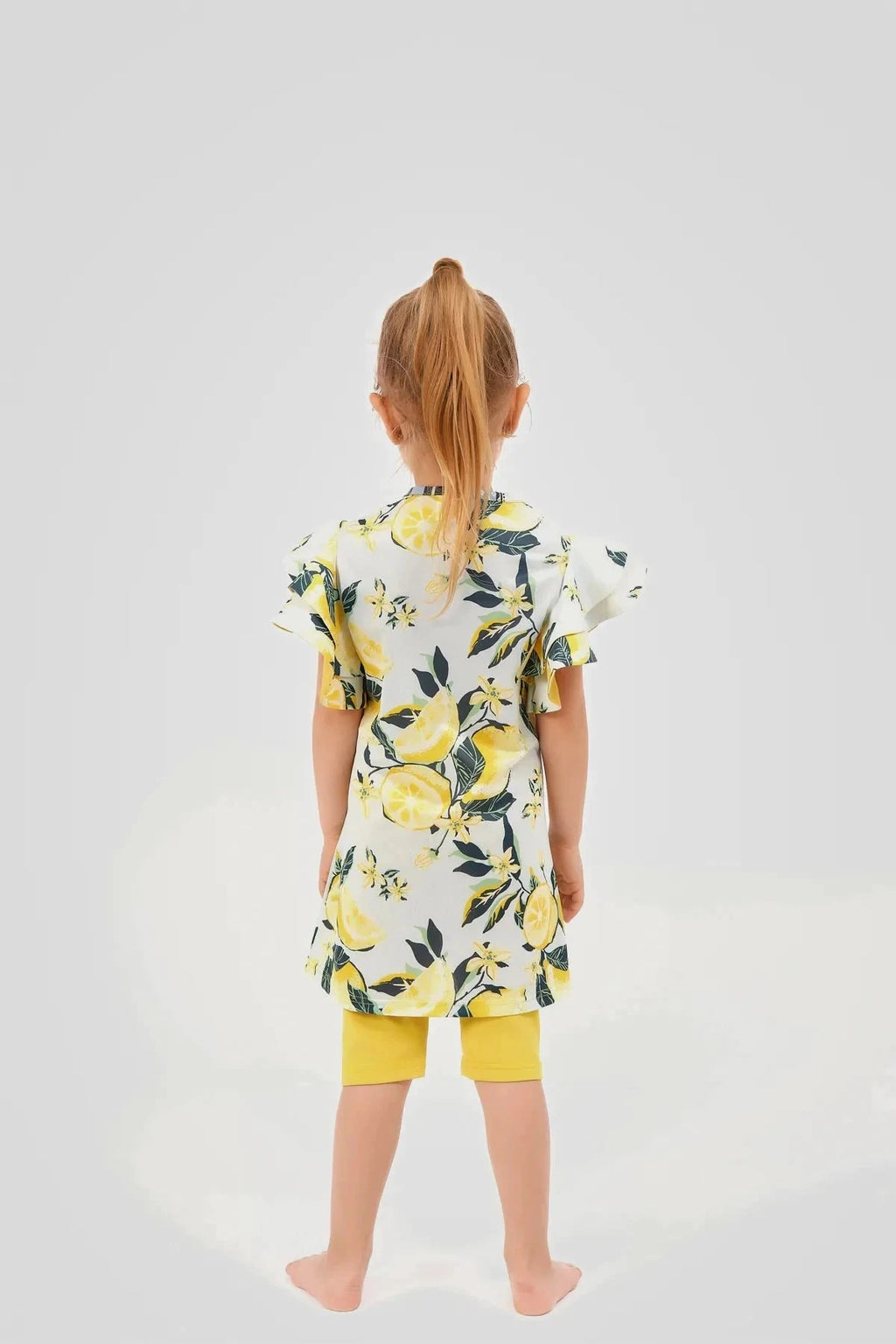 Back view of a girl in a lemon print modest swim dress and yellow shorts
