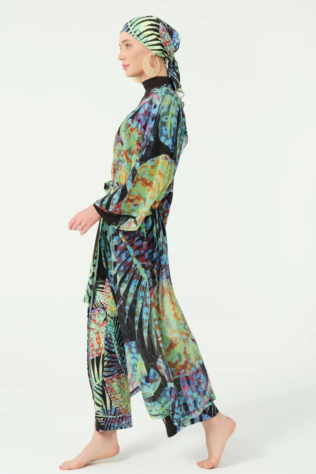 Side profile of model in multi-color sheer kimono and black modest swimwear.