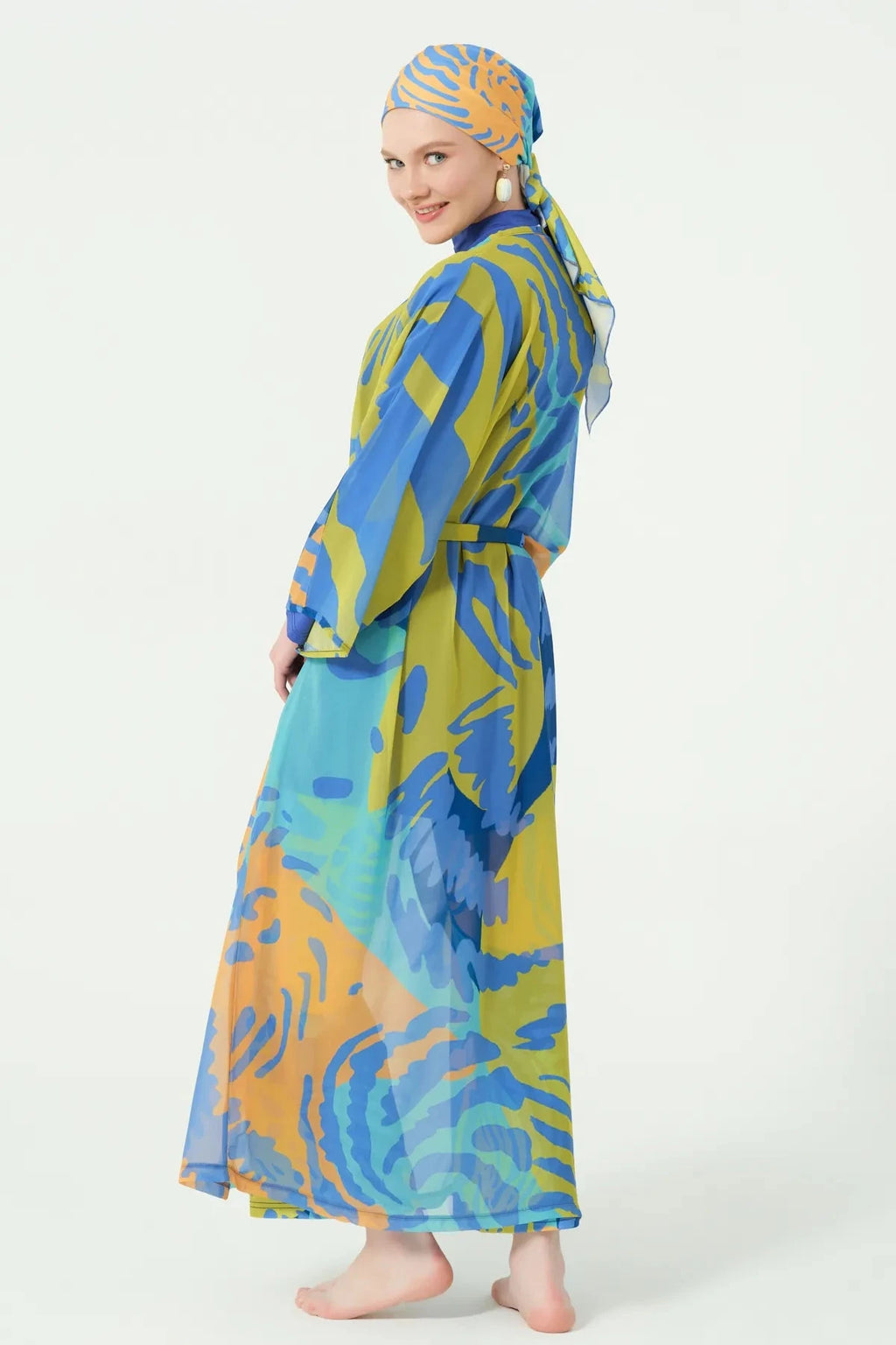 Woman in tropical print kimono with belt and head covering, side view looking back.