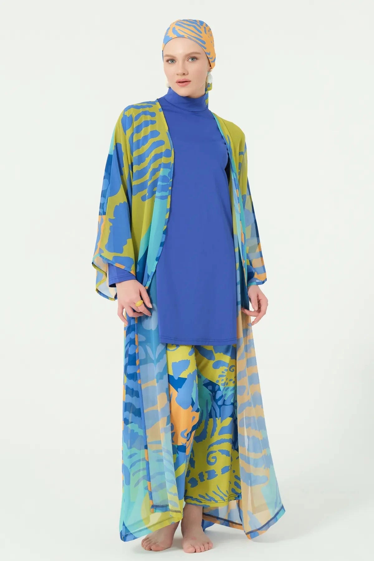 Woman in tropical print kimono open, showing blue full coverage swimsuit underneath.