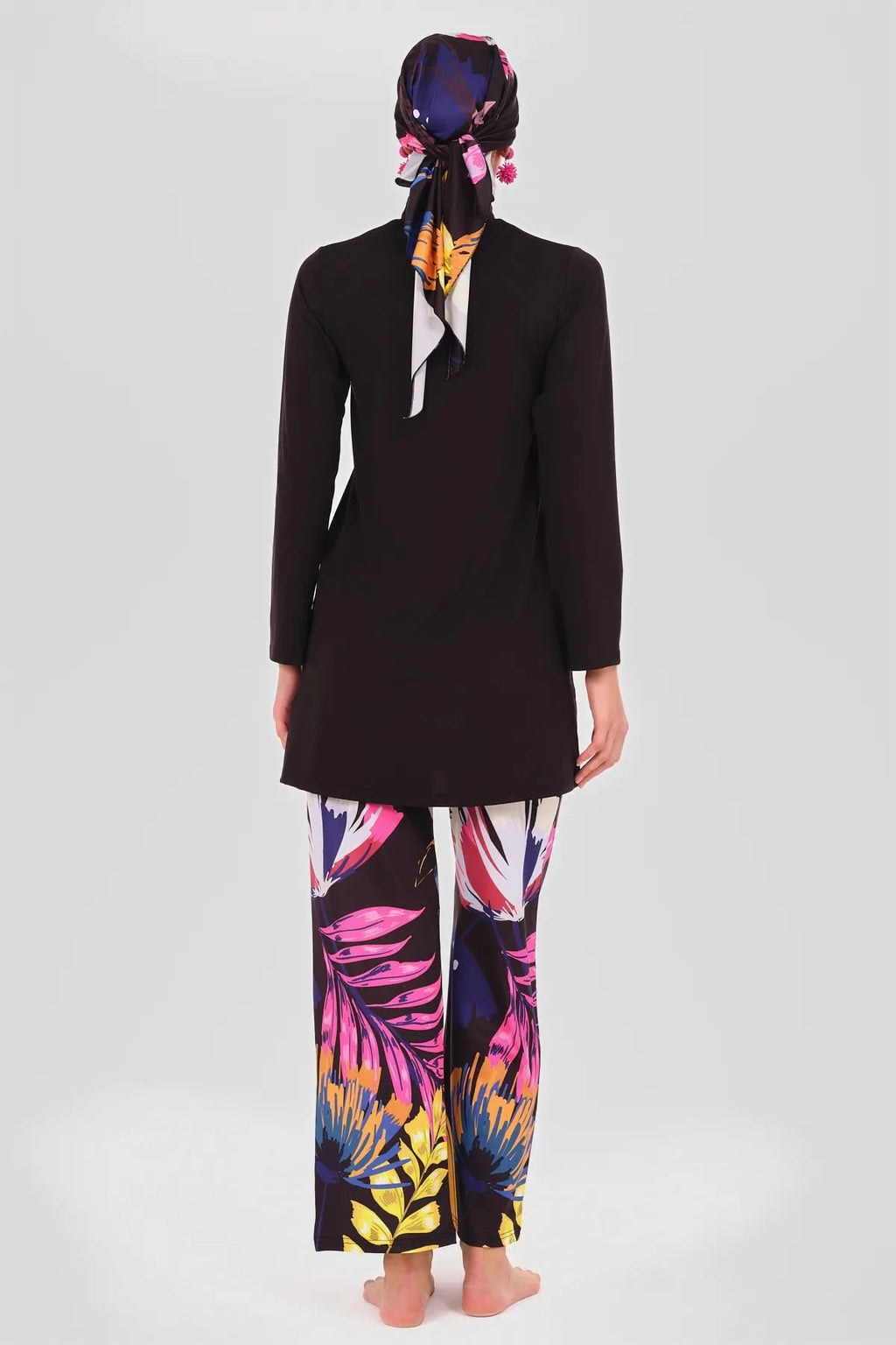 Model in black tunic, floral pants, and headscarf, back view.