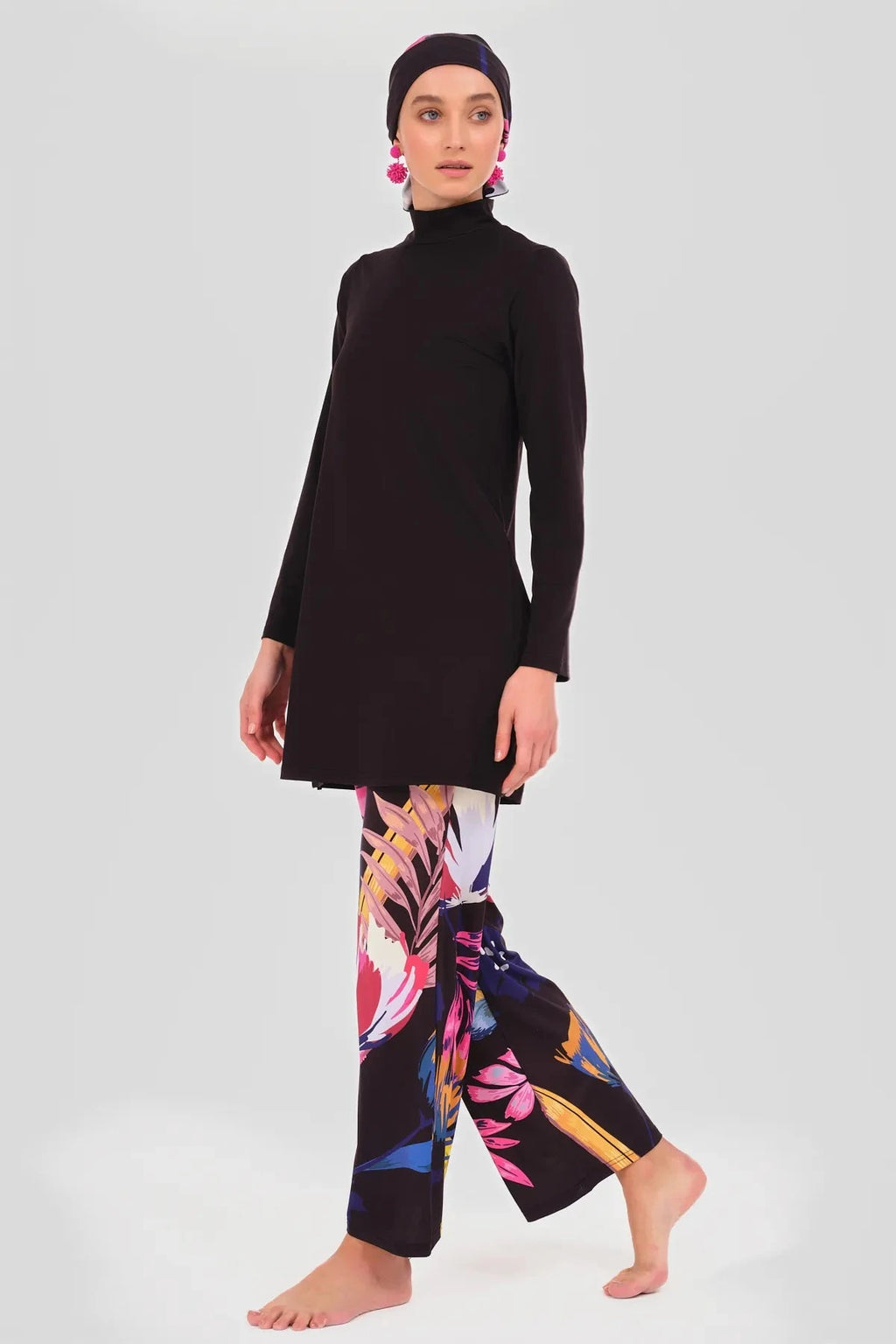 Model in black tunic, floral pants, and headscarf, side walking pose.