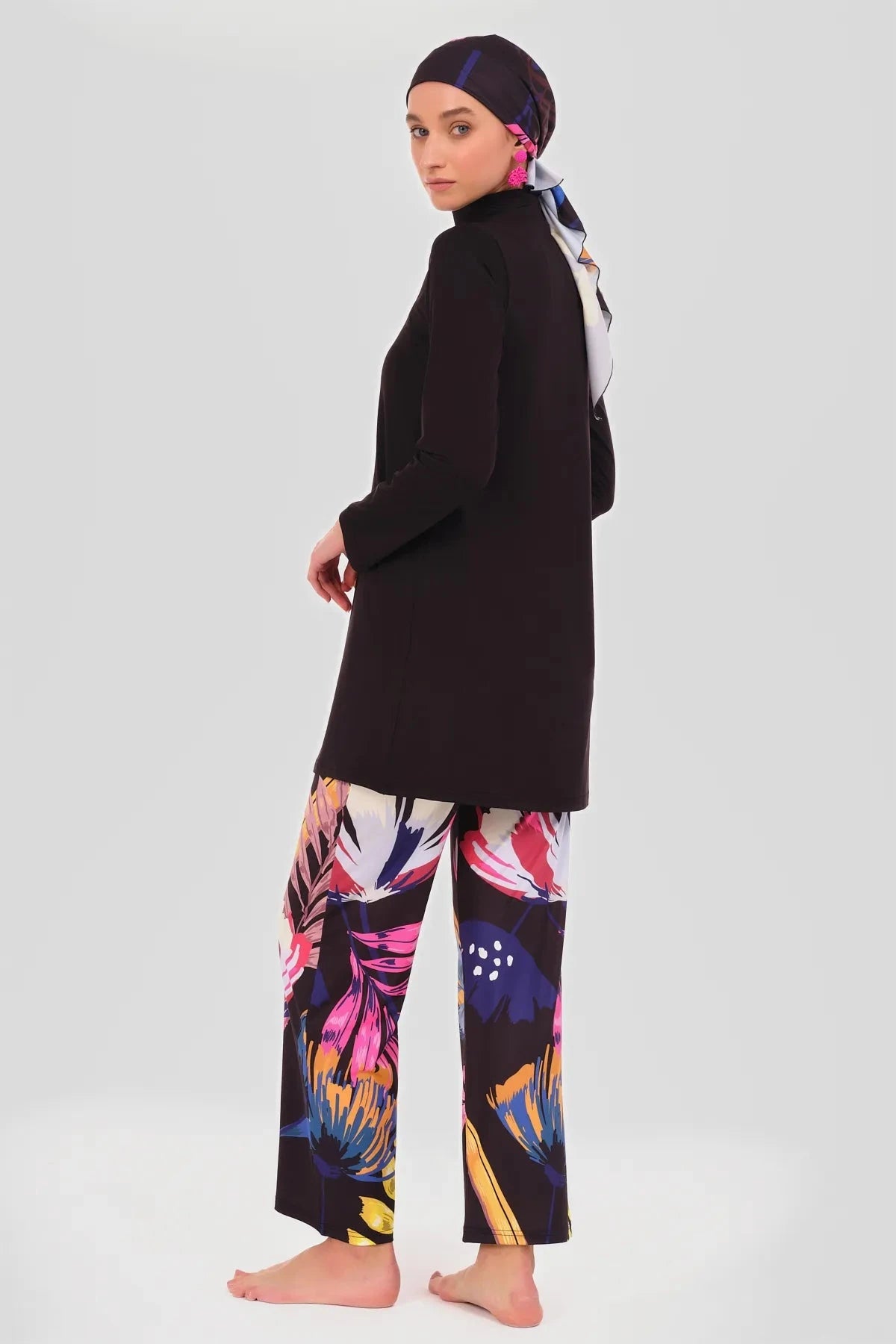 Model in black tunic, floral pants, and headscarf, side profile.