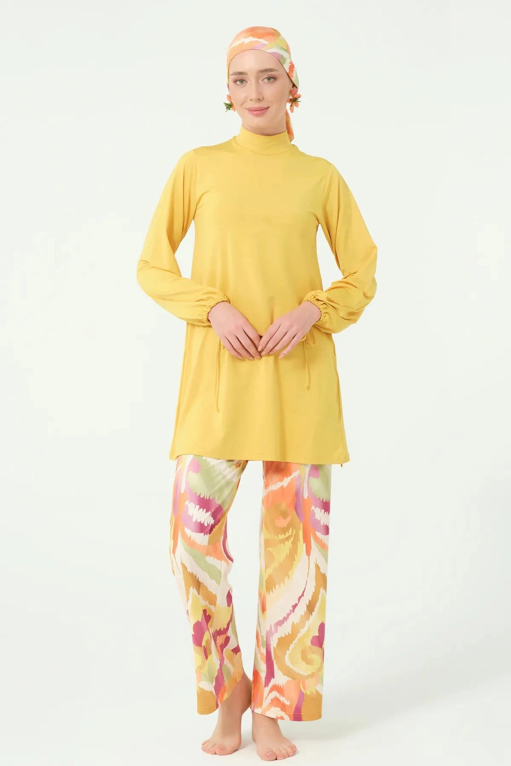 Model in golden-yellow burkini top and abstract print swim pants, front view.