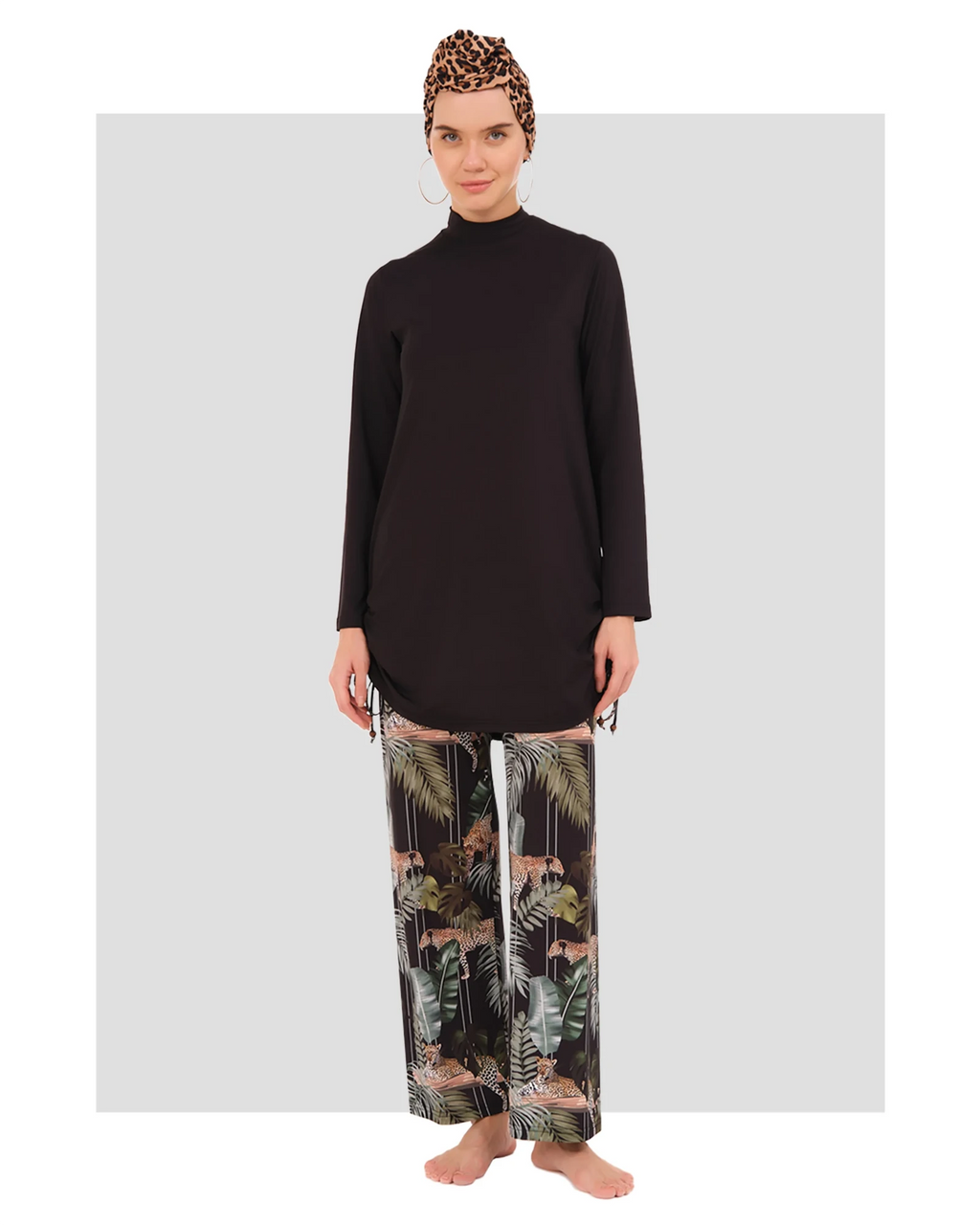 Woman in black modest tunic, tropical print pants, leopard headscarf front view.