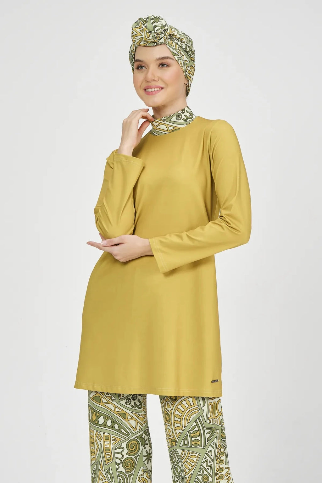 Model in mustard yellow top and green patterned head covering smiling.