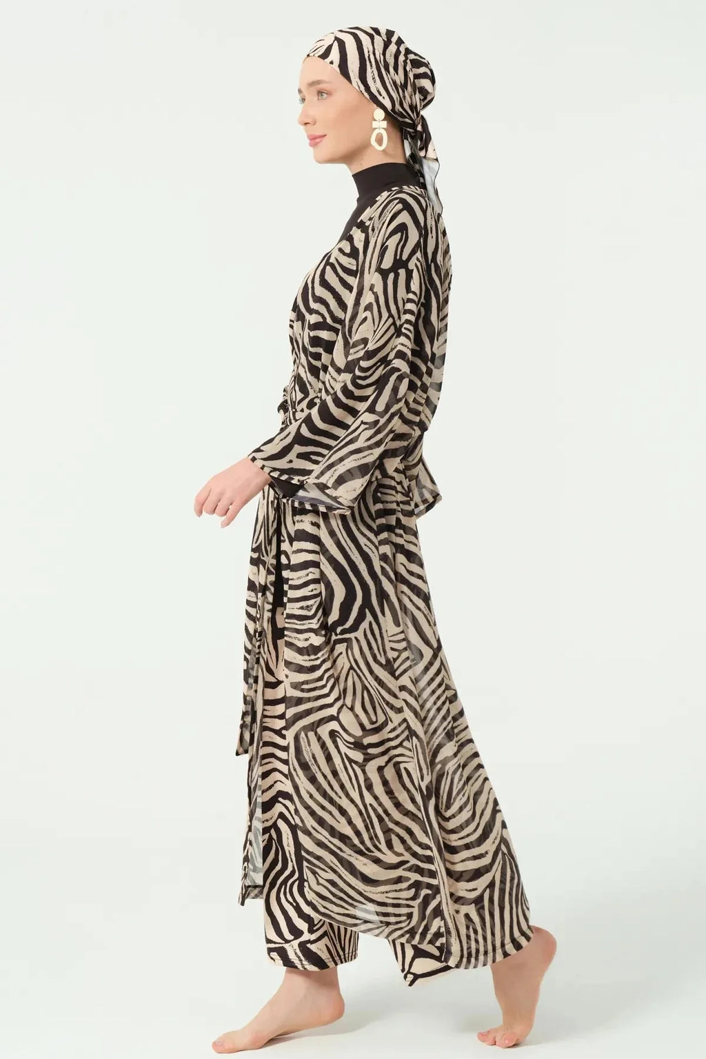 Model walking in zebra print sheer kimono over black modest swimwear, side view.