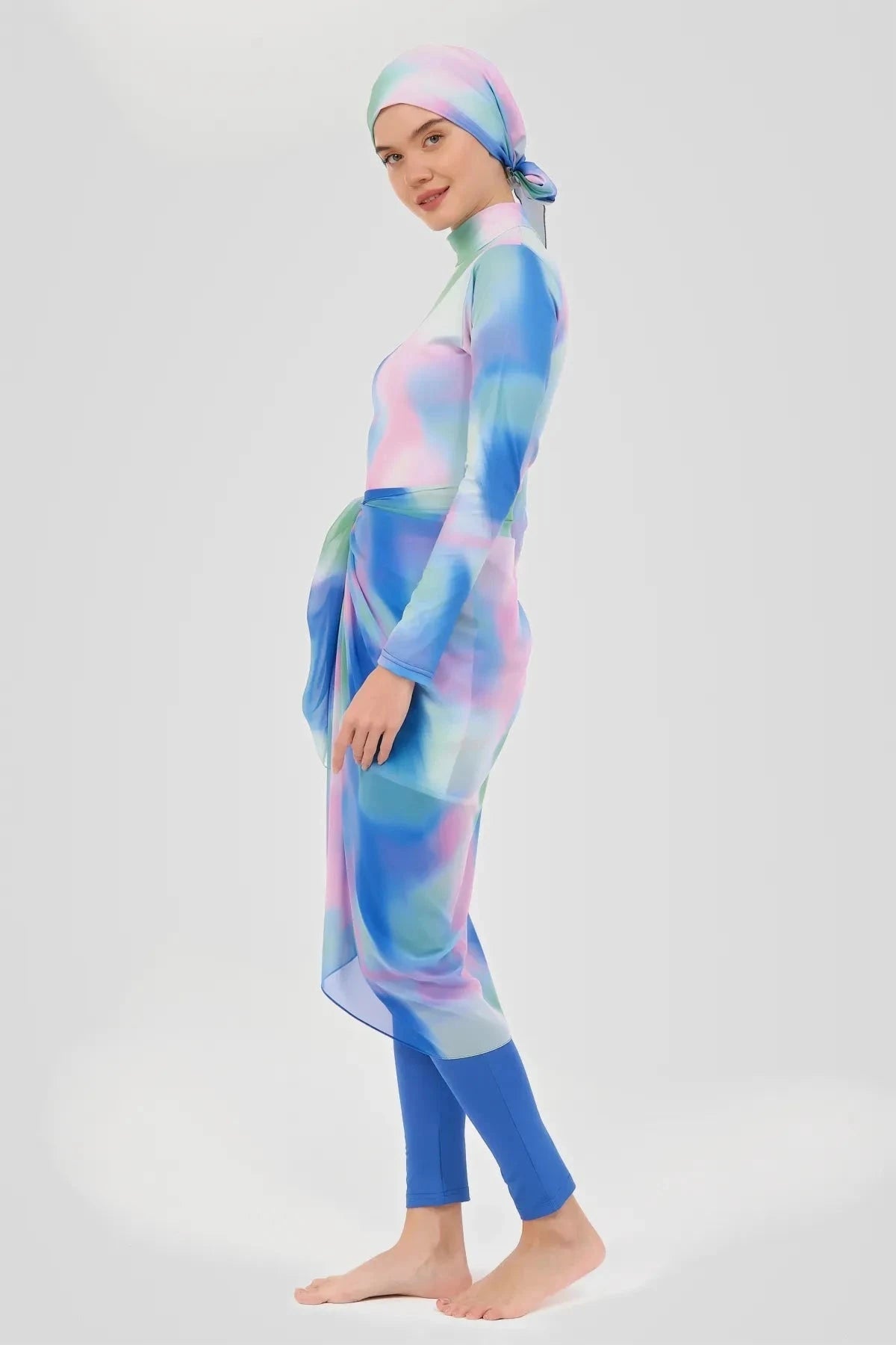 Model wearing pastel tie-dye modest sarong with blue swimsuit, side view.